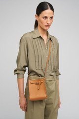 Profile view of model wearing the Oroton Margot Tiny Bucket Bag in Dark Camel and Smooth Leather Lining for Women